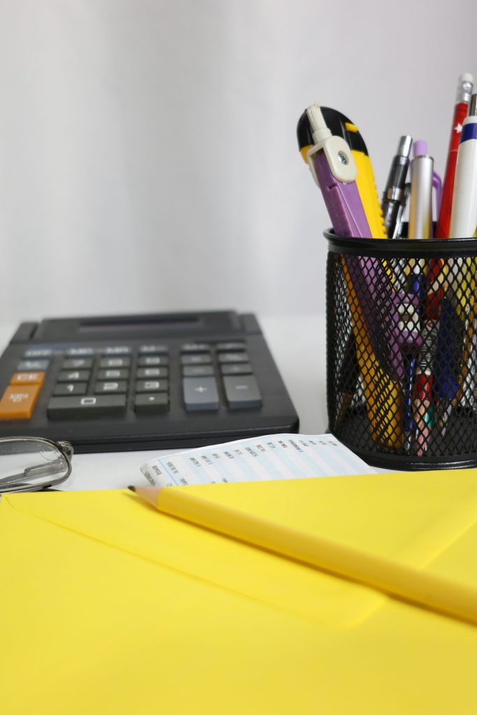 Escritorio con calculadora, bolígrafos y sobre amarillo.